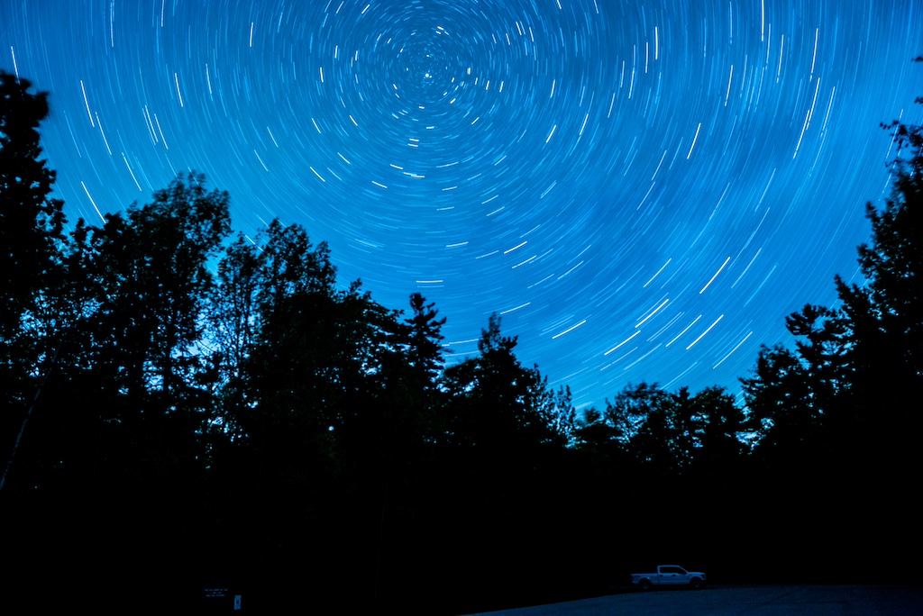 North Star in long-exposure shot. silhouette of trees under blue sky