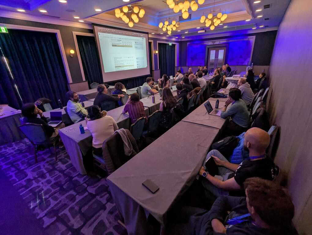 Meeting room with 40 or so people sitting and a presentation on the projector