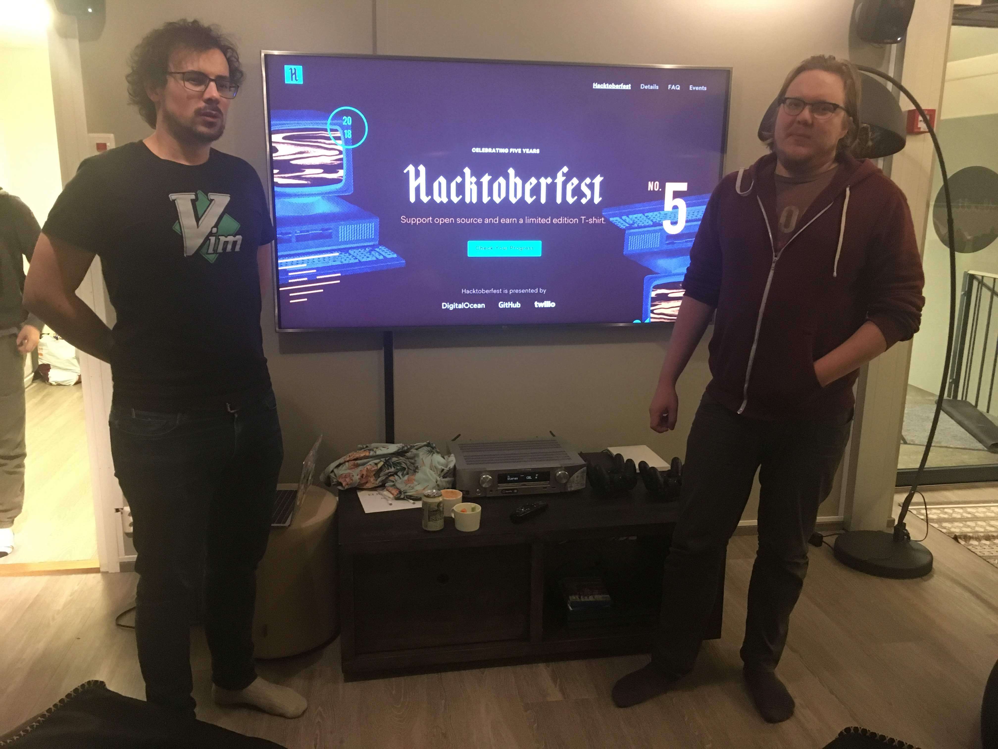 Joonas and Thibaud, standing on each side of the big screen, present Hacktoberfest to the audience. They look happy.
